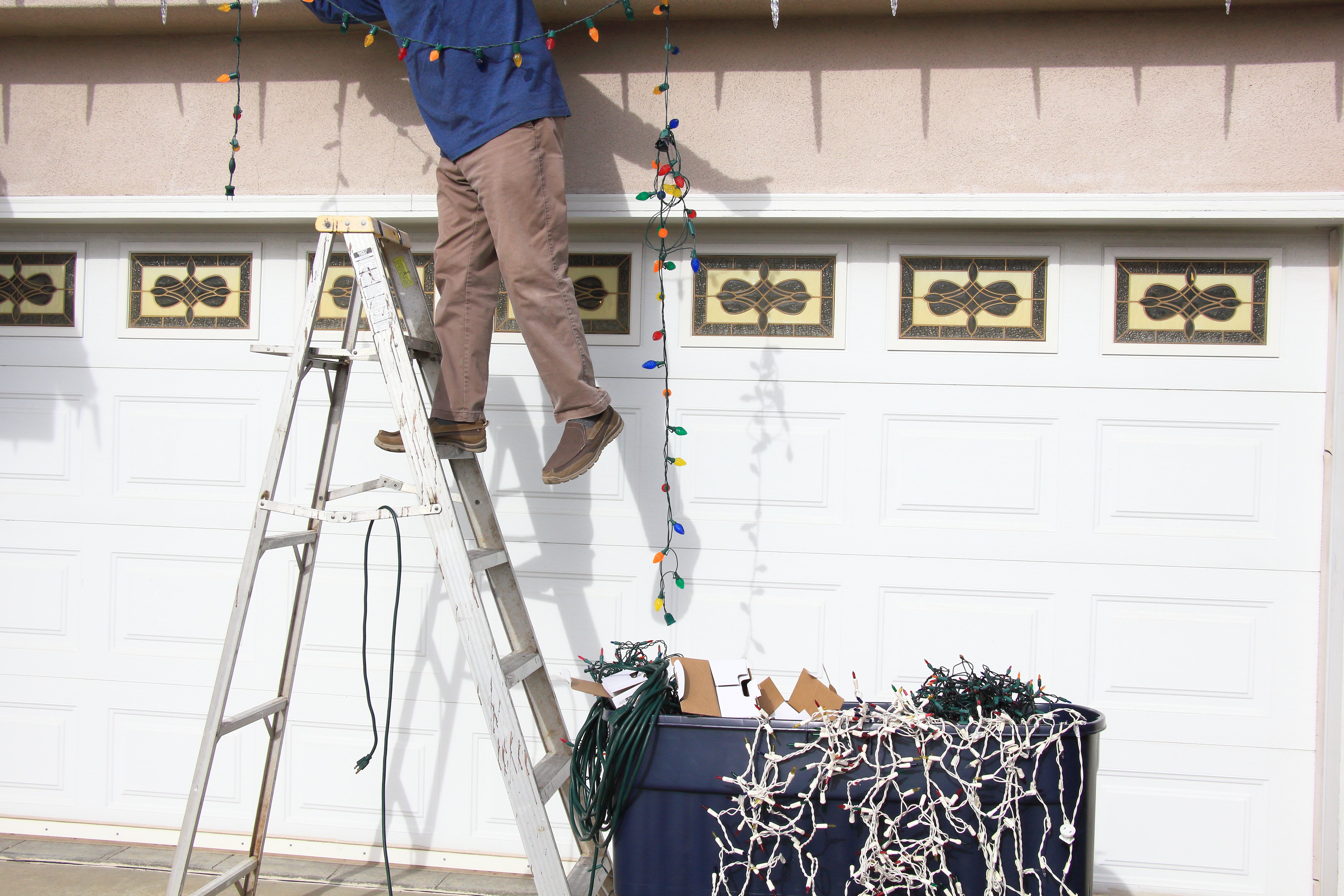 Person on a ladder hanging Christmas lights in front of garage. 